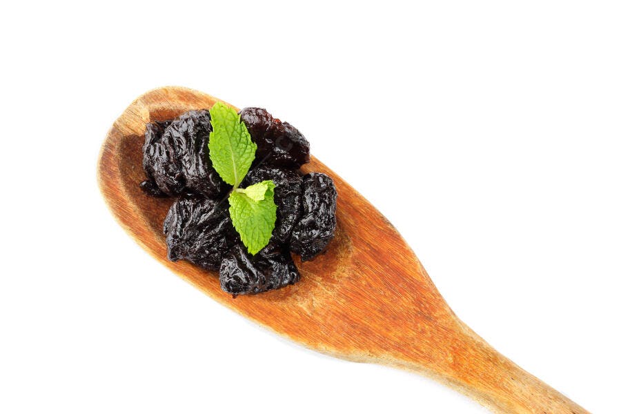 Ameixas secas na colher de madeira com hortelã fresca