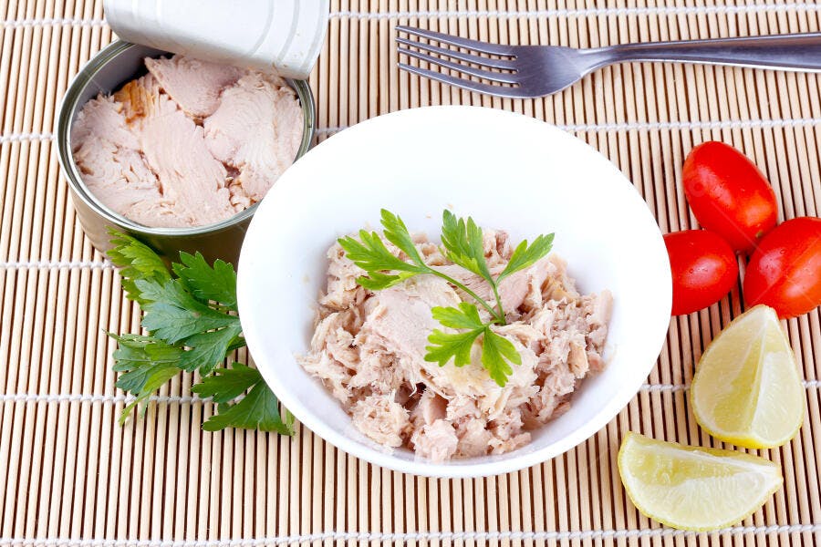 Atum enlatado em tigela branca com salsa, tomate e limão em esteira de bambu