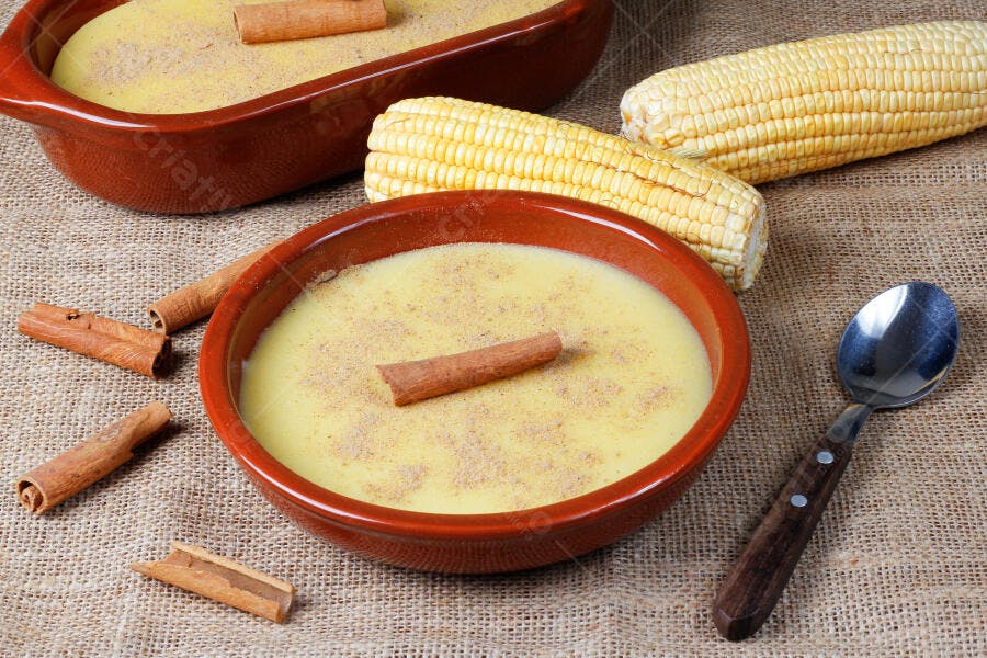 Curau de milho cremoso em tigelas de barro com milho espigas e canela em mesa rústica