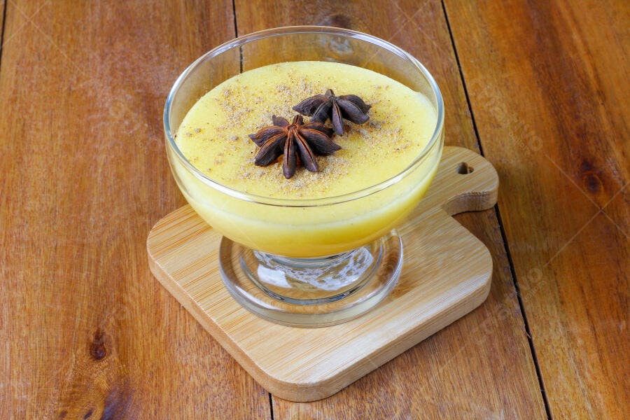 Curau de milho cremoso amarelo com anis estrelado em mesa de madeira rústica