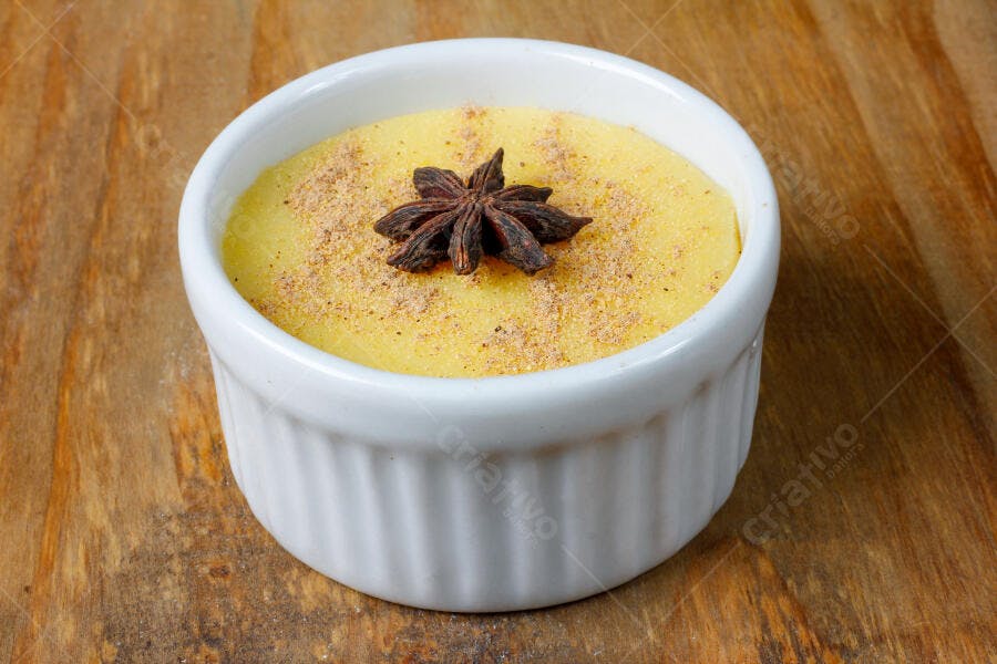Doce cremoso amarelo com anis estrelado e canela em tigela branca sobre madeira rústica
