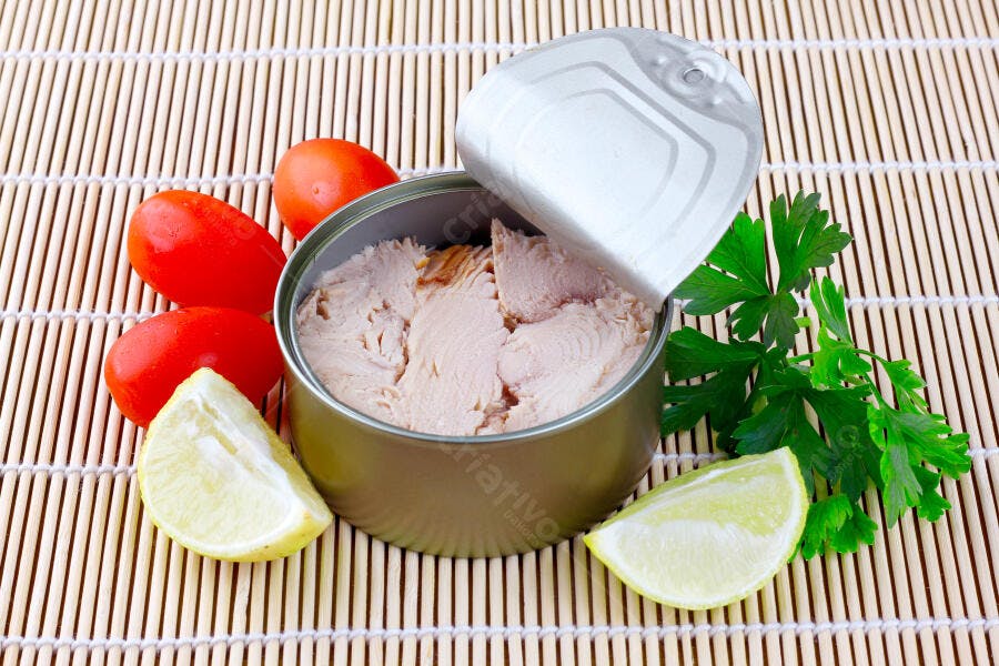 Lata de atum aberta com limões frescos e tomates cereja sobre esteira de bambu