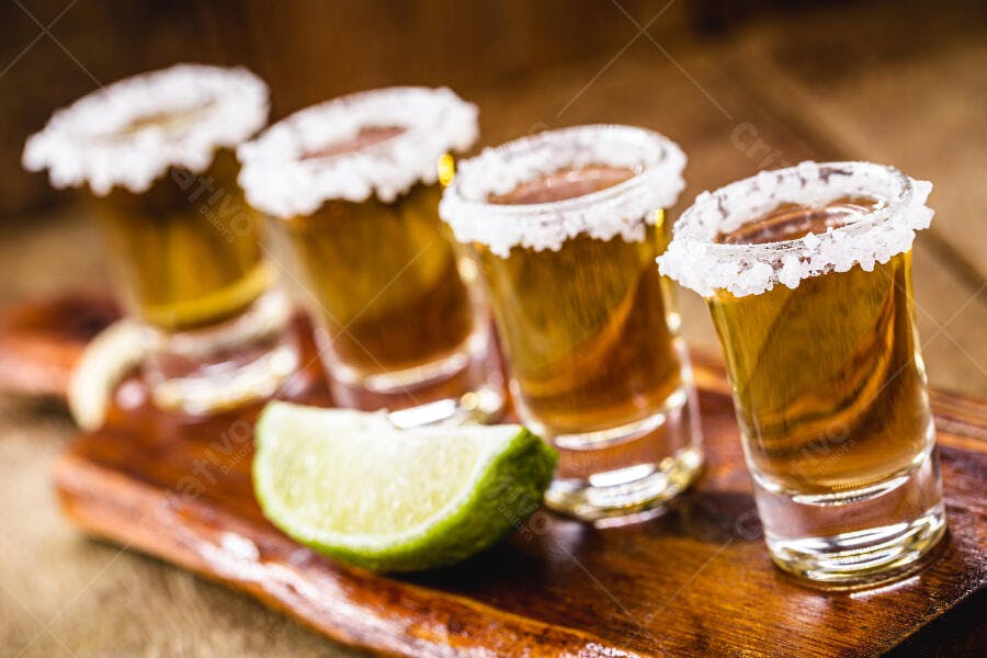 Quatro doses de tequila com sal e limão em tábua de madeira rústica festa