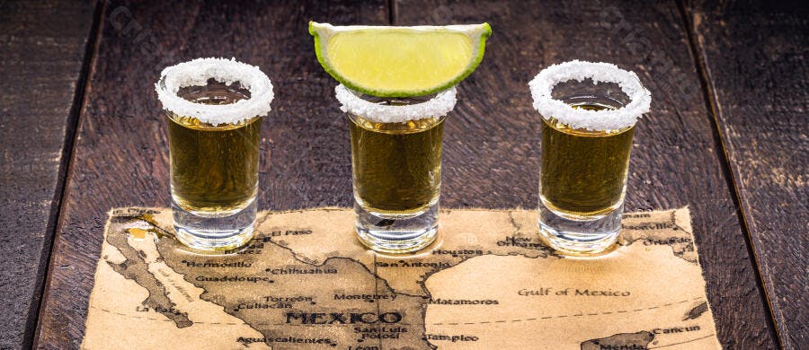 Três shots de tequila com sal e limão sobre mapa do México em madeira escura