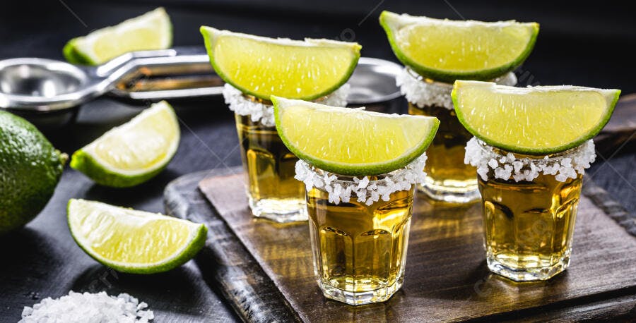 Tequila shots dourados com sal e limão fatiado em fundo escuro