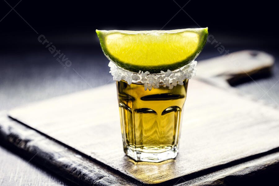 Copo de shot de tequila com borda de sal e limão fresco em ambiente escuro