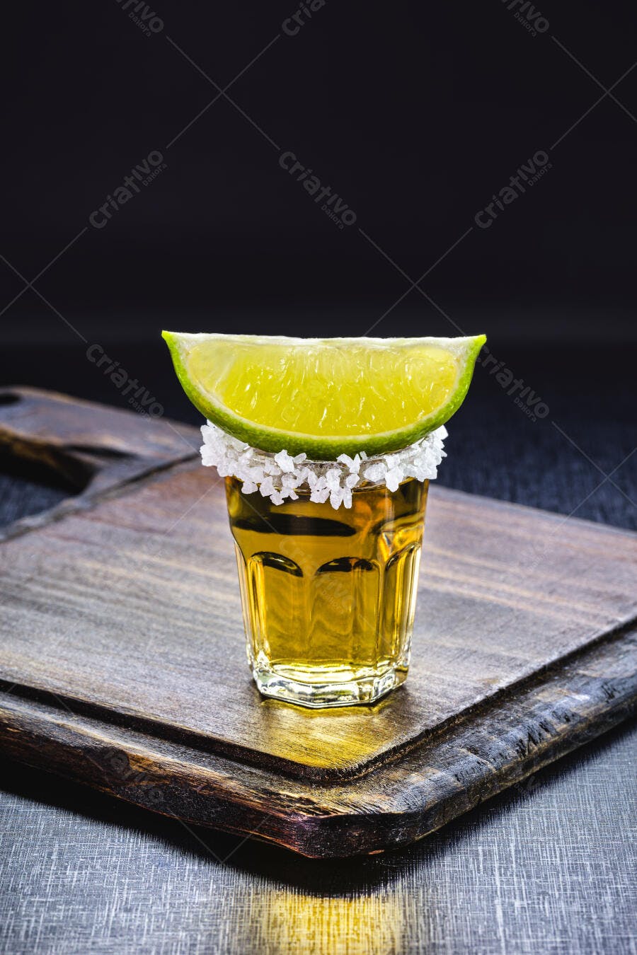 Tequila dourada com limão verde e sal em copo pequeno sobre tábua rústica