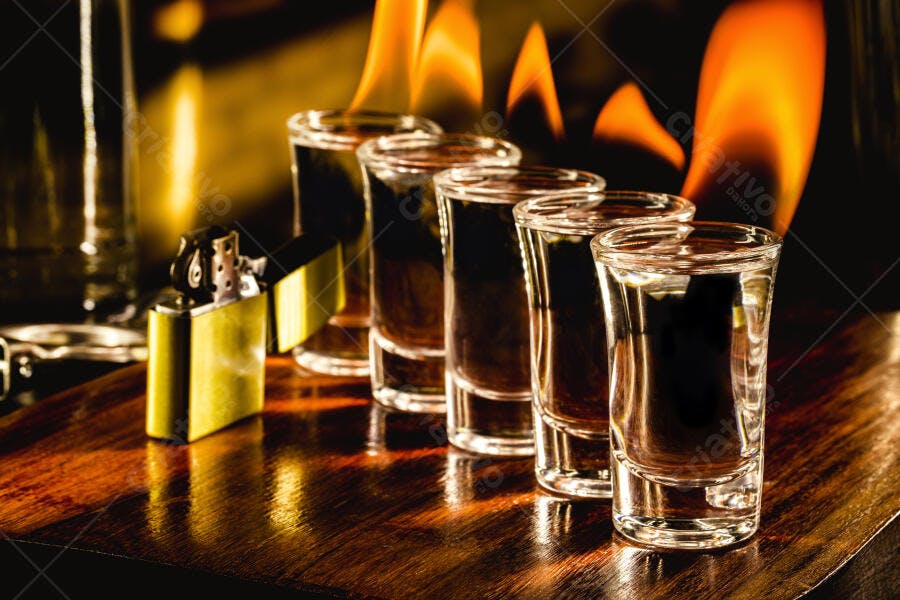 Shots de bebida com isqueiro dourado e chamas em fundo escuro