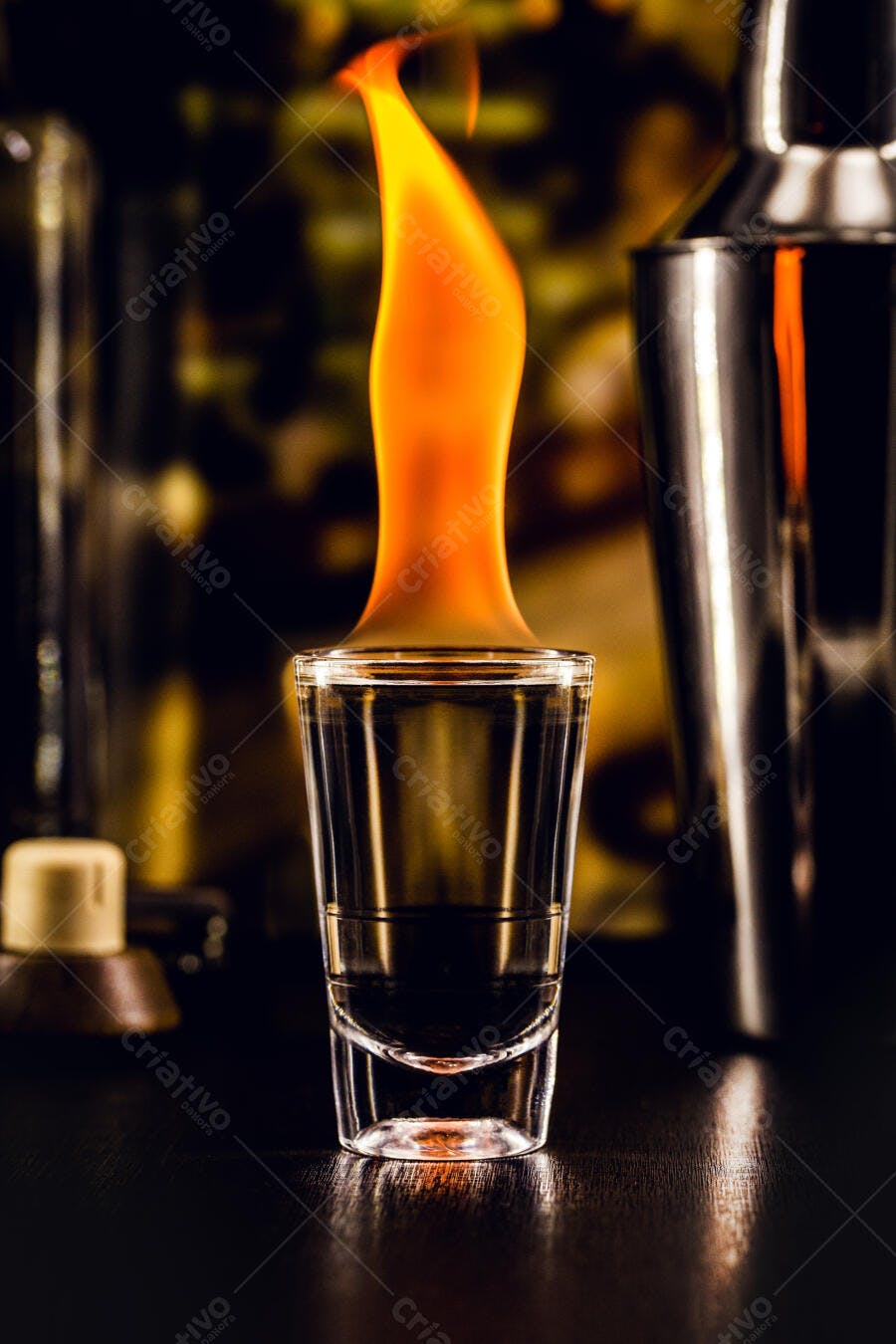Copo shot com coquetel flamejante em balcão escuro de bar