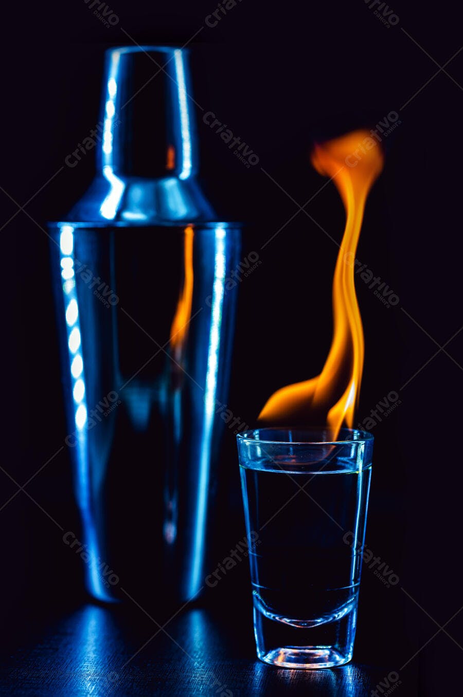 Copo de shot com coquetel flamejante e coqueteleira azul neon em fundo escuro
