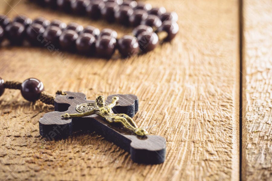 Rosário marrom com crucifixo dourado em mesa de madeira rústica