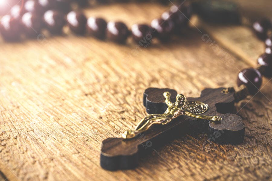 Rosário e crucifixo de madeira com Cristo dourado em superfície rústica