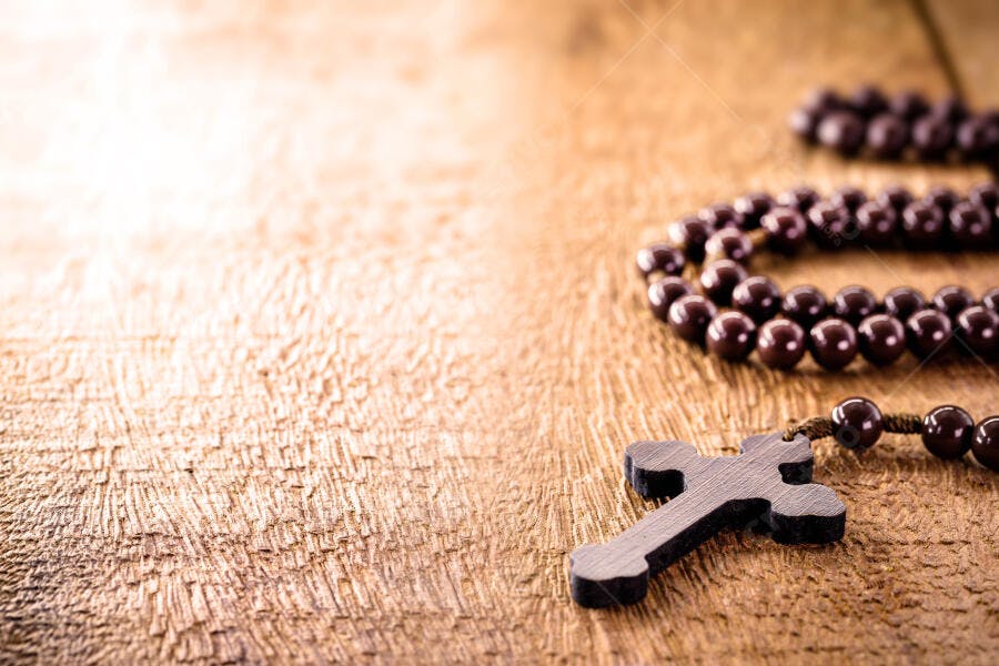 Terço com crucifixo de madeira escura sobre superfície rústica marrom