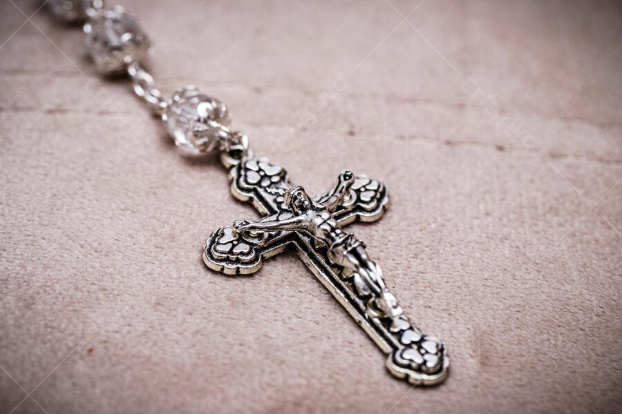 Rosário católico com crucifixo prateado e contas de cristal em fundo bege
