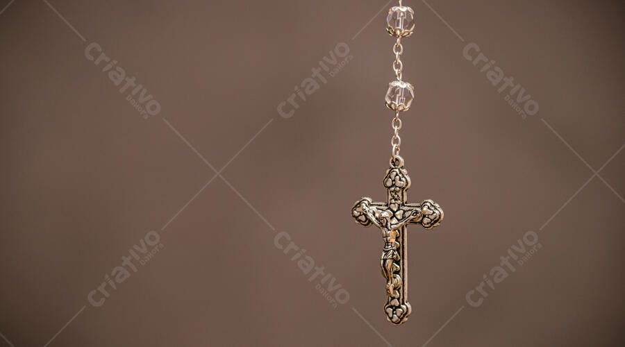 Rosário prateado com crucifixo detalhado e contas transparentes em fundo marrom neutro