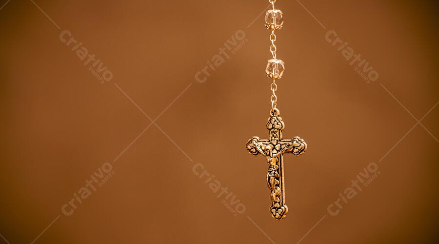 Rosário dourado com crucifixo detalhado em fundo marrom escuro