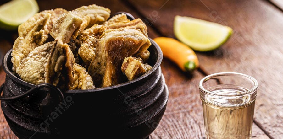 Torresmo crocante em panela de ferro com cachaça e limão na mesa rústica
