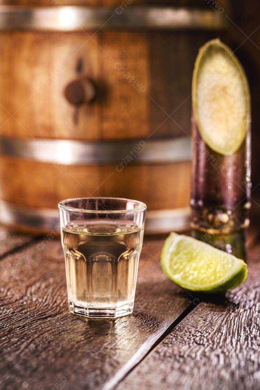 Copo de cachaça com limão e cana de açúcar em barril de madeira rústico