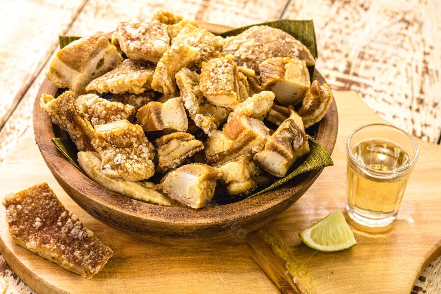 Torresmo crocante em tigela de madeira com cachaça e limão na mesa rústica