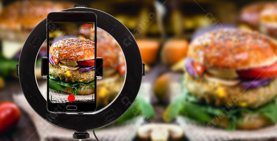 Hambúrguer vegano com alface e tomate sendo gravado por smartphone com ring light