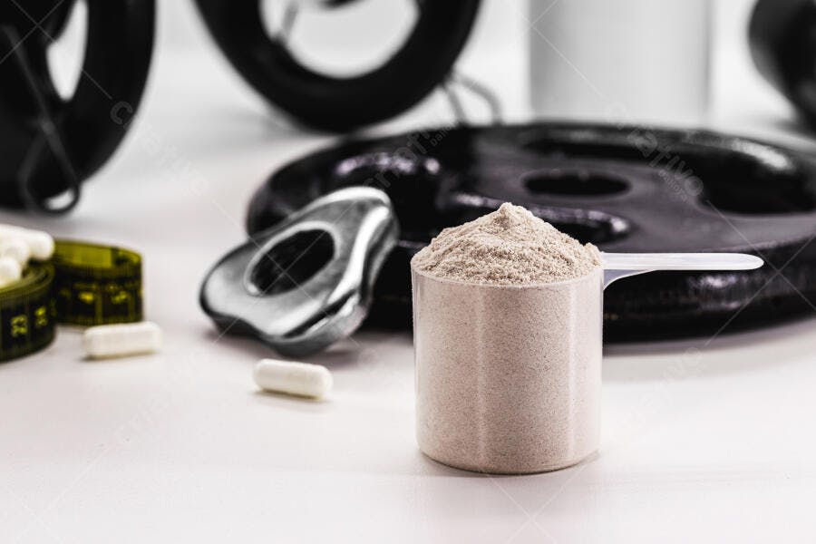 Scoop de proteína em pó bege com pesos de academia e medidor de fita em fundo branco