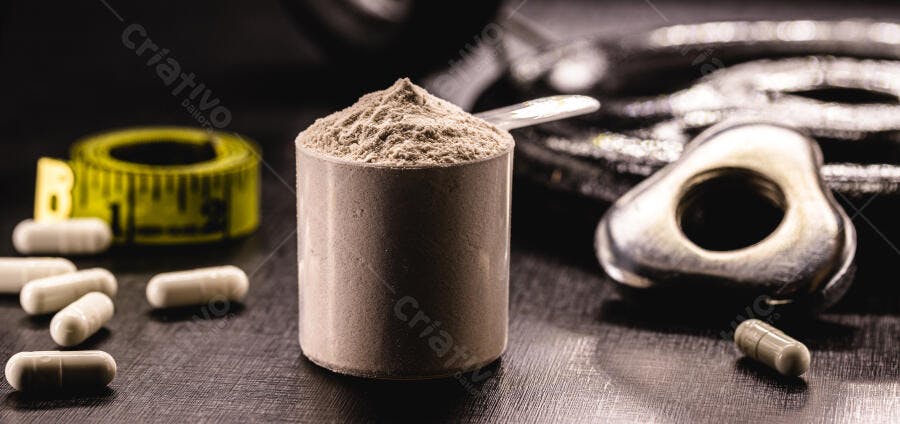 Copo de whey protein com suplementos e fita métrica em fundo escuro de academia