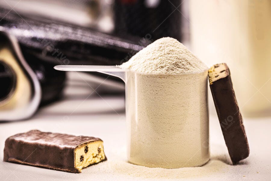 Whey protein pó branco na colher medidora e barras de chocolate fitness