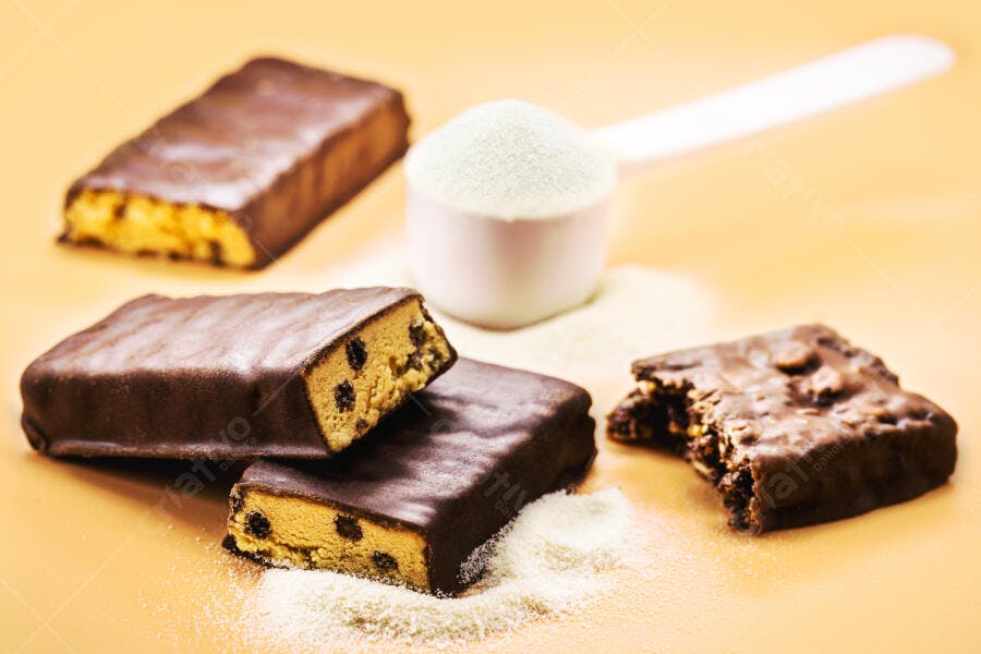 Barras de proteína de chocolate e scoop de pó em fundo laranja para fitness