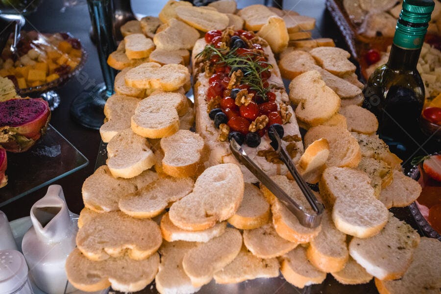 Tábua de pães fatiados com patê branco tomate mirtilo e alecrim em buffet