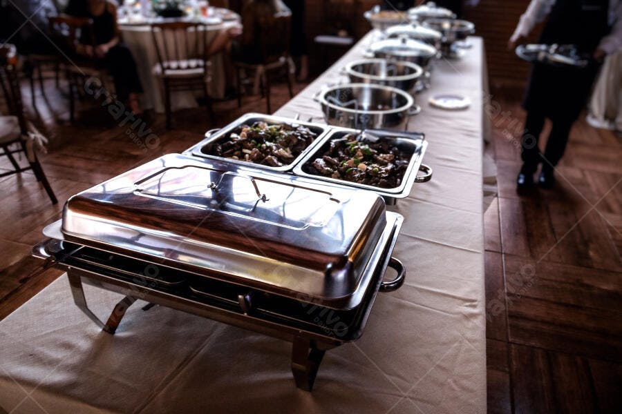 Catering buffet com chafing dishes prateados e carne em evento elegante