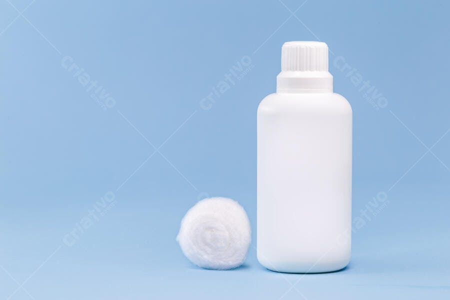 Garrafa plástica branca e bola de algodão em fundo azul claro, produto de higiene