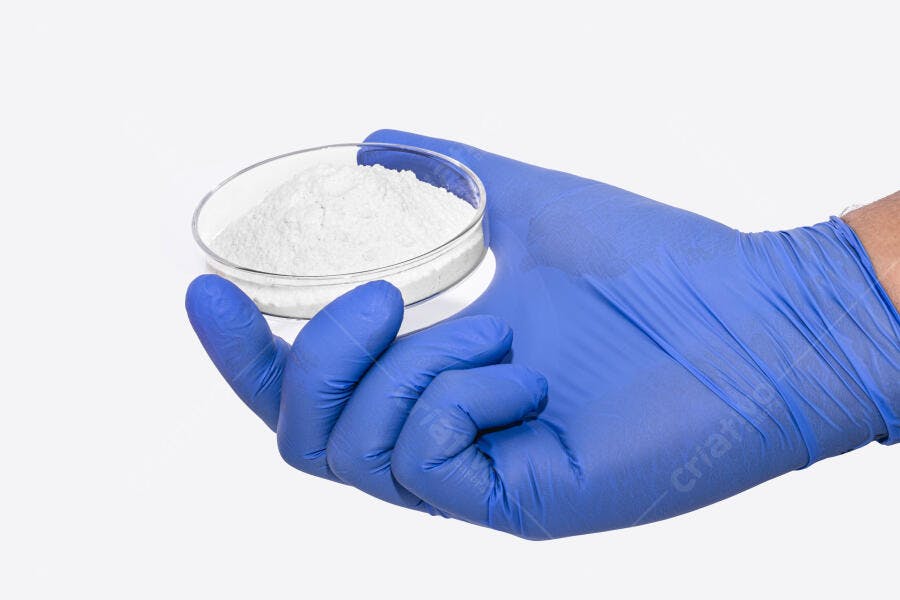 Mão com luva azul segurando placa de Petri com pó branco em laboratório