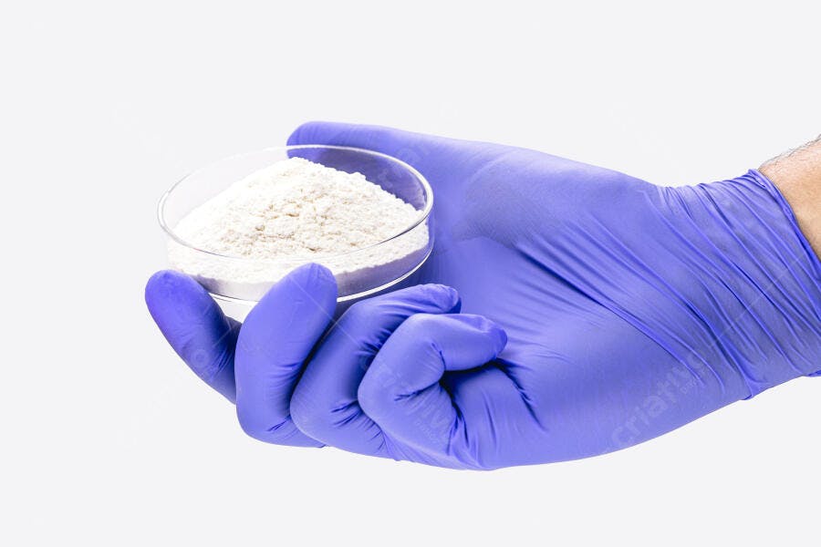 Mão com luva roxa segurando placa de petri com pó branco em laboratório