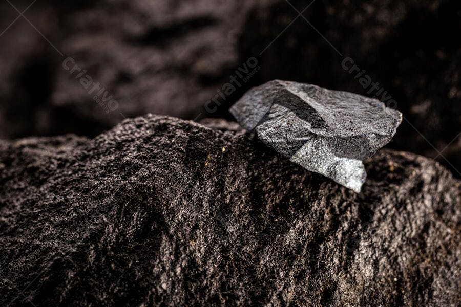 Carvão mineral cinza escuro sobre superfície rochosa preta áspera