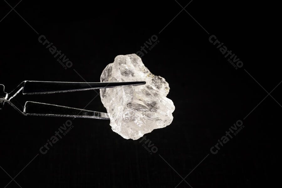 Cristal bruto transparente segurado por pinça metálica em fundo preto de estúdio