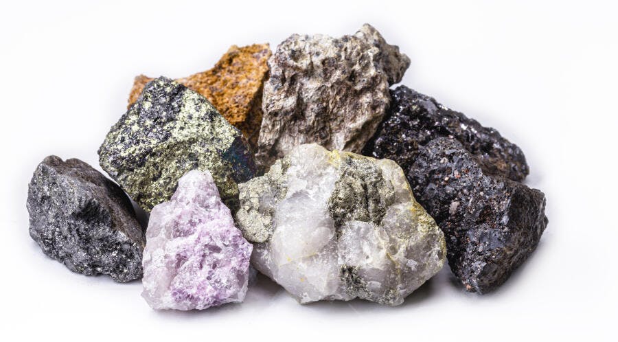 Minerais brutos variados em tons de dourado roxo cinza e preto em fundo branco
