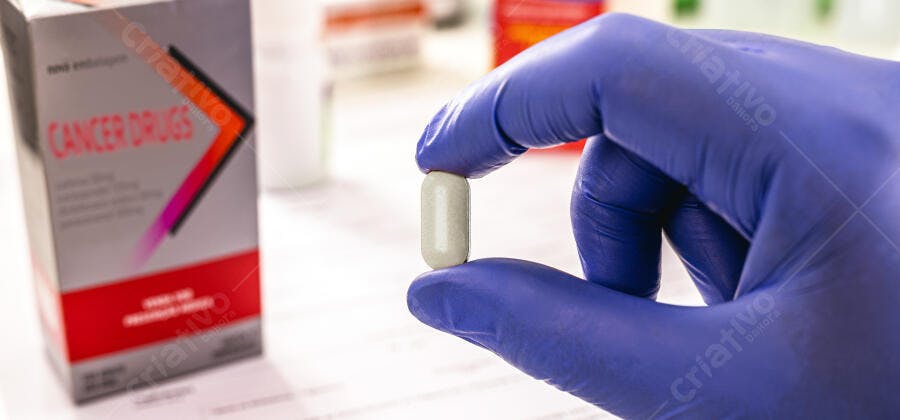 Profissional com luva azul segurando cápsula medicamento para câncer