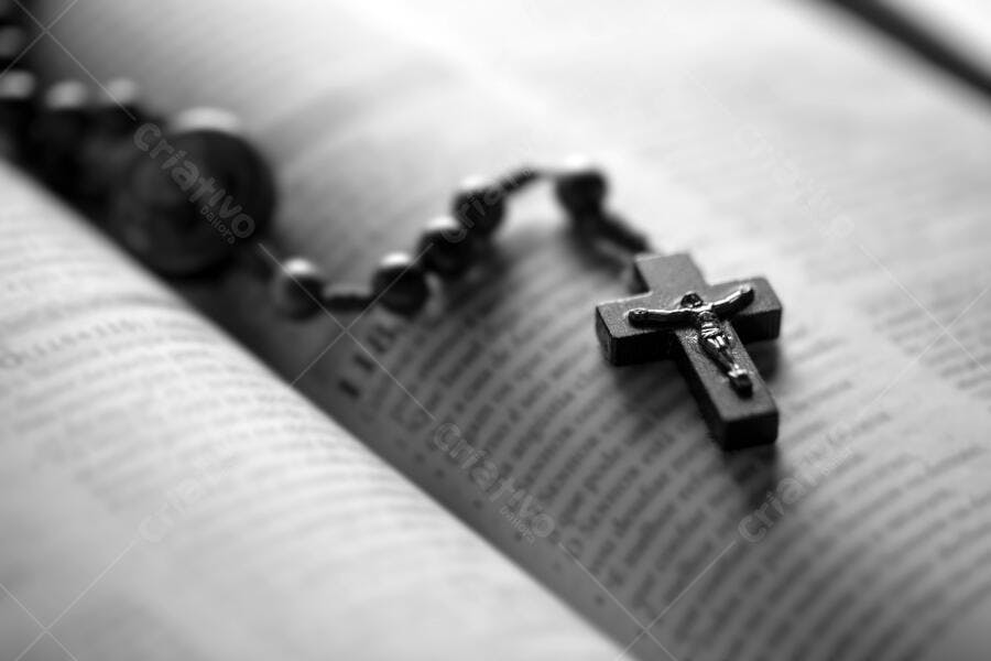 Rosário com crucifixo cinza sobre Bíblia aberta em preto e branco