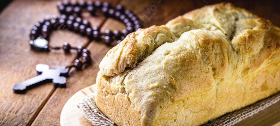 Pão caseiro rústico e rosário cristão sobre madeira