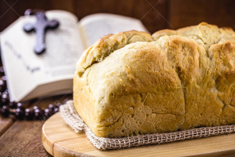 Pão caseiro dourado na tábua de madeira com Bíblia e terço