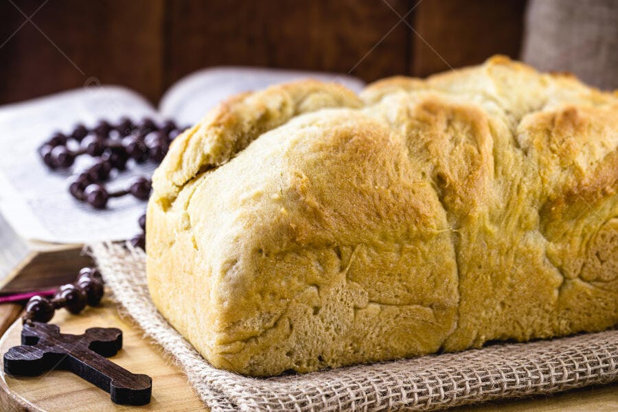 Pão caseiro rústico com bíblia aberta e terço em mesa de madeira