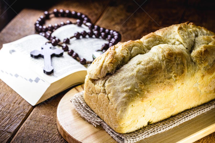 Pão caseiro com bíblia e rosário em mesa rústica de madeira
