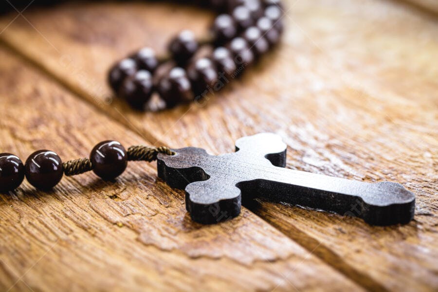 Rosário de madeira escura com crucifixo sobre mesa rústica de madeira