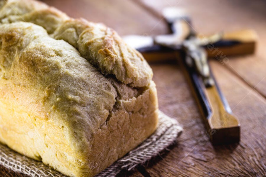 Pão caseiro dourado com crucifixo de madeira e toalha rústica marrom em mesa de madeira