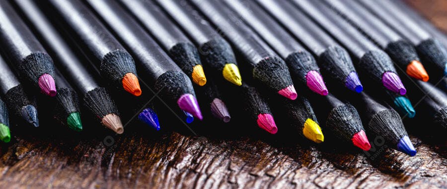 Lápis de cor pretos com pontas coloridas vibrantes sobre madeira