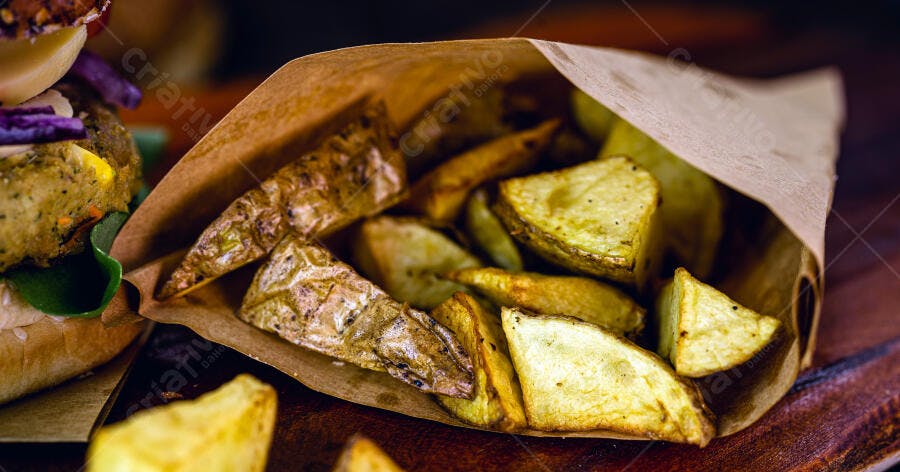 Batatas rústicas douradas em saco de papel ao lado de hambúrguer