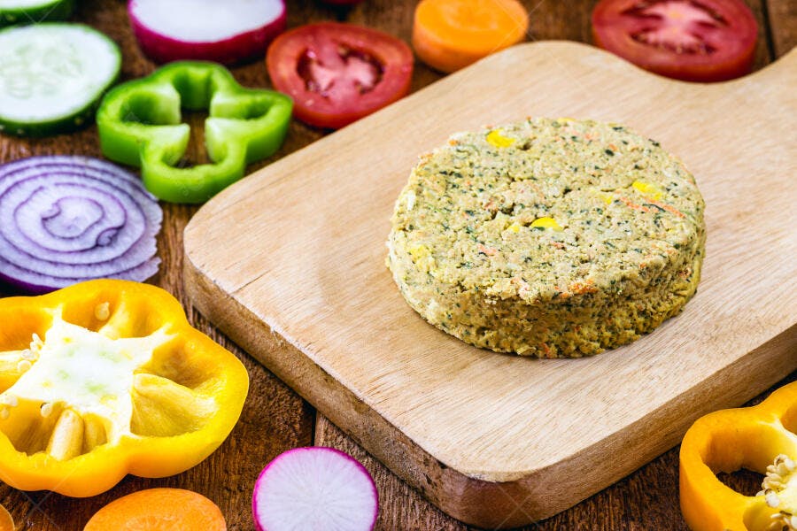 Hambúrguer vegano verde com milho e vegetais coloridos em tábua de madeira