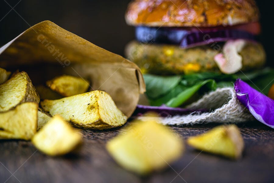 Hambúrguer vegano com batatas rústicas em saco de papel sobre mesa escura