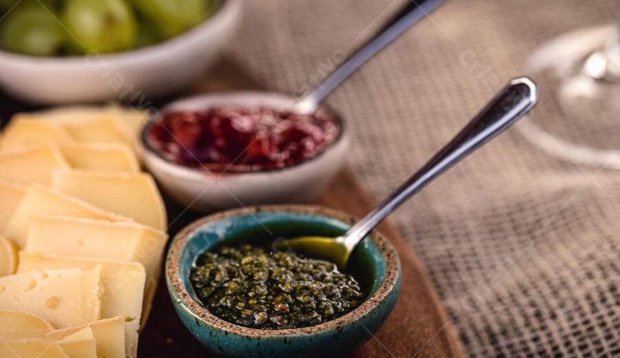 Queijo fatiado com pesto verde e geleia vermelha sobre mesa rústica