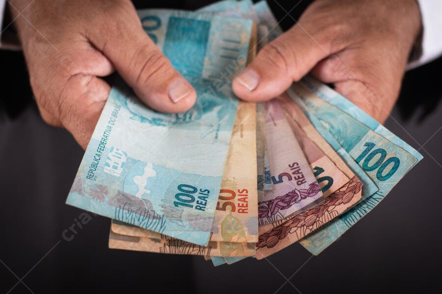 Homem segurando notas de Reais brasileiras 100, 50 e 5 reais